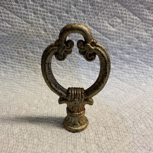Puede incluir: Tirador de mueble ornamentado de estilo antiguo, con acabado dorado y bronce. El tirador presenta un diseño de bucle decorativo con detalles florales y una base detallada, adecuado para armarios o cajones.