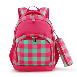 May include: A pink and green plaid backpack with a matching pencil case. The backpack has a large main compartment and a smaller front pocket. The pencil case is attached to the side of the backpack with a zipper.