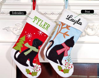 Peut inclure: Deux chaussettes de Noël avec des revers blancs. La chaussette rouge présente un chien noir portant une écharpe rayée verte et blanche, un sapin vert et le nom brodé TYLER. La chaussette bleu clair présente un chat noir avec une écharpe rayée rouge et blanche et le nom imprimé Layla.