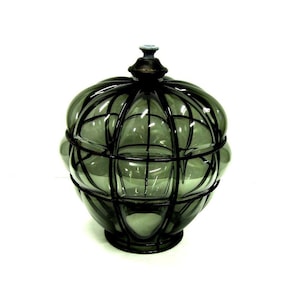 Puede incluir: Un tarro de vidrio decorativo con tapa. El tarro es de color verde ahumado y tiene un dise&ntilde;o similar a una jaula hecho de metal oscuro. La tapa est&aacute; rematada con un peque&ntilde;o adorno ornamental. El tarro se asienta sobre una base redonda.