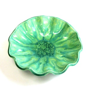 May include: A green ceramic bowl with a wavy rim and a flower-like design in the center.