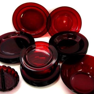 May include: A collection of ruby red glass dishware, including plates, bowls, and a divided serving dish. The set features various sizes and shapes, all in a deep, translucent red color. The arrangement suggests a complete dining set.