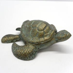 May include: A bronze-colored turtle figurine with a textured shell and flippers. The turtle has a weathered appearance with green and gold tones. The figurine is a decorative item, likely for home decor.