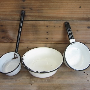 May include: Three white enamelware kitchenware items with black rims. A large bowl and two dippers with black handles.