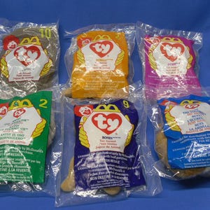 May include: Six colorful plastic bags with Ty Beanie Babies inside. Each bag has a different color and features a different Beanie Baby. The bags are labeled with the Beanie Baby's name and a McDonald's logo.