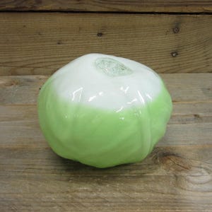 May include: A white and green glass cabbage shaped ornament. The ornament is made of glass and has a white top and a green bottom.