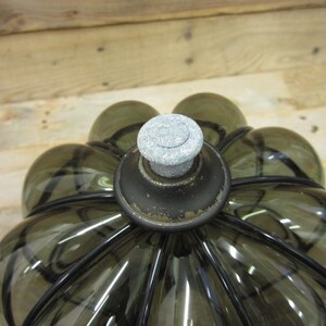 Puede incluir: Una botella decorativa de vidrio con un tono verde oliva oscuro y una forma redondeada &uacute;nica. La botella presenta un tap&oacute;n de piedra gris y detalles met&aacute;licos negros. El dise&ntilde;o recuerda a una flor.