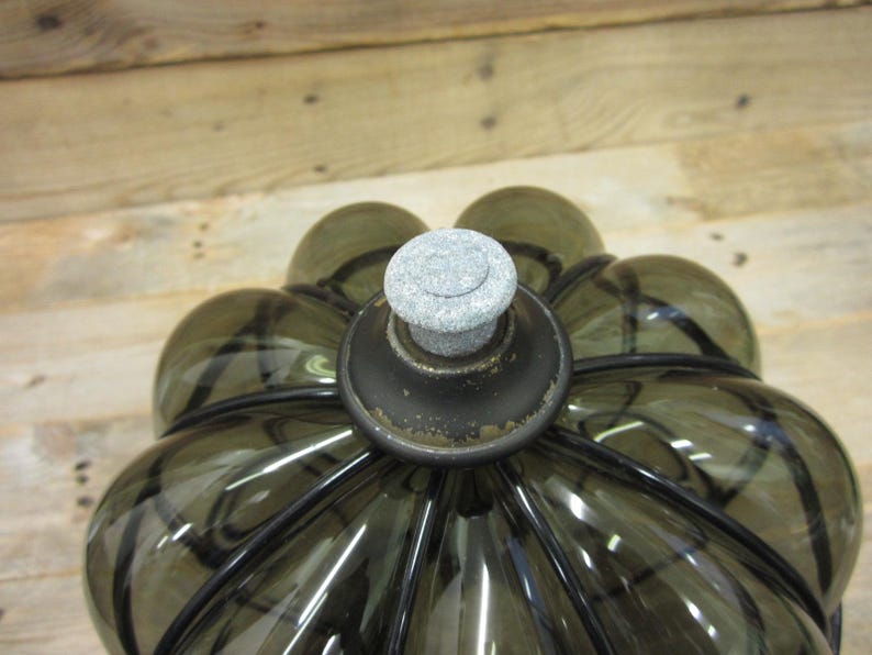 Puede incluir: Una botella decorativa de vidrio con un tono verde oliva oscuro y una forma redondeada &uacute;nica. La botella presenta un tap&oacute;n de piedra gris y detalles met&aacute;licos negros. El dise&ntilde;o recuerda a una flor.