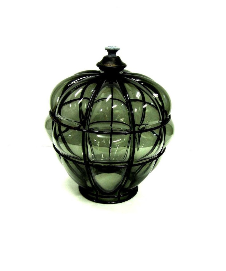 Puede incluir: Un tarro de vidrio decorativo con tapa. El tarro es de color verde ahumado y tiene un dise&ntilde;o similar a una jaula hecho de metal oscuro. La tapa est&aacute; rematada con un peque&ntilde;o adorno ornamental. El tarro se asienta sobre una base redonda.