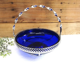 May include: A vintage cobalt blue glass basket with a silver-toned metal handle and filigree rim. The handle has a twisted design with blue accents. The basket is likely used for serving or display.
