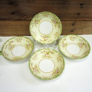 May include: Four antique porcelain bowls with a floral design. The bowls have a cream-colored base with a gold rim and a green border. The floral pattern includes pink and yellow flowers.