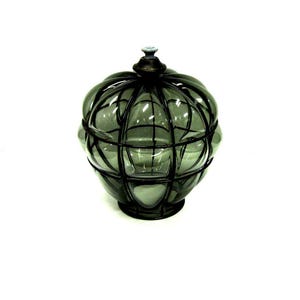 Puede incluir: Un tarro de vidrio decorativo con un dise&ntilde;o de jaula de metal oscuro. El tarro es de color verde apagado y tiene forma redonda con tapa. La jaula de metal a&ntilde;ade una est&eacute;tica vintage o antigua.
