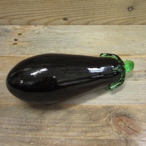May include: A black glass eggplant with a green glass stem. The eggplant is shiny and has a smooth surface.