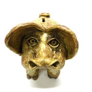 May include: A ceramic piggy bank shaped like a pig's head with a large snout and brown and tan glaze.