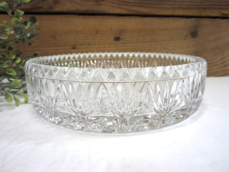Op de afbeelding: Een heldere, ovale glazen kom met een gedetailleerd, gestructureerd patroon. De kom heeft een geschulpte rand en een decoratief ontwerp aan de zijkanten. De kom staat op een wit oppervlak, met een houten achtergrond.