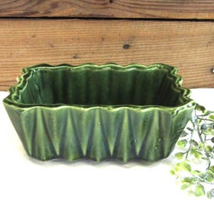 May include: A rectangular ceramic bowl with a glossy dark green glaze and a distinct pleated, accordion-style texture along the exterior walls. The bowl features a scalloped top edge and a deep interior basin, showcasing a uniform finish throughout.