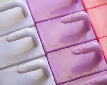 May include: Close-up of ceramic tiles in white, lavender, and pink. Each tile has a curved handle shaped like a finger. The tiles are arranged in a grid pattern, creating a visually interesting and artistic display.