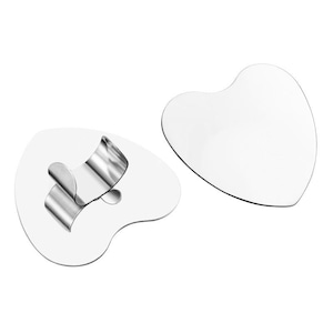 Op de afbeelding: Twee hartvormige, witte cosmetische tools. Eén heeft een gebogen, zilveren metalen handvat. De andere is een effen hartvorm. De tools zijn waarschijnlijk voor gezichtsmassage of huidverzorging.