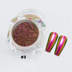 May include: A clear jar containing shimmering, reddish-brown nail powder, marked with the number "#3". Two iridescent, oval-shaped nail tips are to the right. The tips reflect a gradient of pink, yellow, and green.