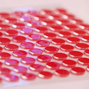 Puede incluir: Primer plano de una cuadrícula de pequeñas baldosas de vidrio redondas y rojas. Las baldosas están dispuestas en filas y columnas ordenadas, con una superficie ligeramente elevada y redondeada. El color es un rojo vibrante y brillante.