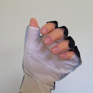 May include: A fingerless glove with a light gray palm and a black trim around the finger openings. The glove has a blue dotted seam along the side. The thumb is exposed. The glove is designed for sports or activities.