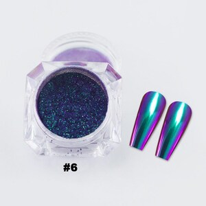 May include: A clear, faceted jar filled with iridescent blue-green powder, next to two long, metallic, colour-shifting nail tips. The jar has a clear lid. The number "#6" is printed in black on the bottom.
