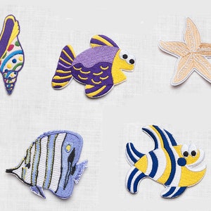 May include: Five embroidered iron-on patches featuring sea life: a seashell, a purple and yellow fish, a starfish, a blue and white fish, and a yellow and blue fish.