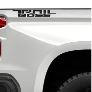 May include: A white pickup truck with a black "TRAIL BOSS" decal on the side. The decal is an officially licensed General Motors product.