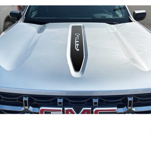 May include: A silver pickup truck with a black hood decal that says "AT4". The truck has a black grille with a GMC logo.