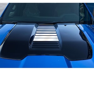 May include: A close-up of a blue truck hood with a black and silver hood scoop. The hood scoop has a series of vertical vents and a silver stripe down the center. The hood scoop is a GM licensed product.