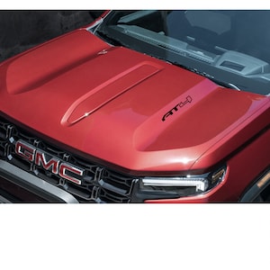 May include: A red GMC Canyon pickup truck with a black "AT4" decal on the hood. The truck has a black grille with a chrome GMC logo.