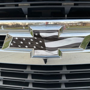 May include: A black and white American flag decal on a silver Chevrolet bowtie emblem.