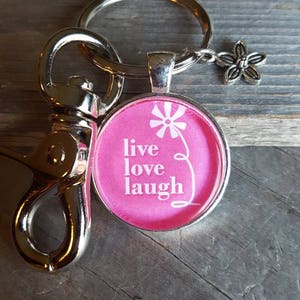 May include: Pink keychain with a silver charm featuring a flower and the words "live love laugh".