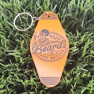 May include: Orange keyring with a black and white illustration of a skeleton with a beard. The keyring has the text "Dads with Beards are Better".