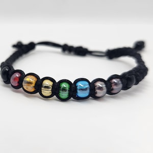 May include: A black cord bracelet with rainbow colored glass beads. The bracelet is tied with a knot and has a small black bead at each end.