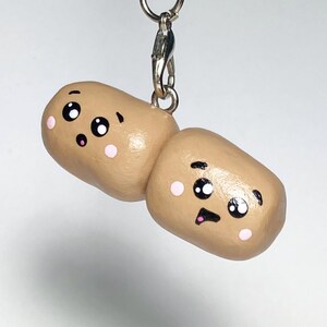 May include: A brown and tan potato-shaped keychain with a cute cartoon face. The keychain has two eyes, a mouth, and two pink cheeks.