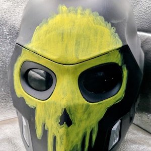 May include: A matte black full-face helmet featuring a hand-painted, bright yellow skull design across the front. The skull graphic has a dripping paint effect around the eye sockets and nose area. The helmet includes two dark, oval-shaped eye visors.