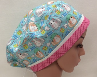 Può includere: Un cappello da lavoro blu e rosa con un motivo di porcellini d'India e articoli per l'igiene dentale. Il cappello ha un laccio bianco e un bordo con motivo rosa e bianco.