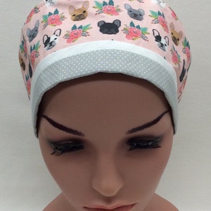 May include: A pink and white scrub hat with a pattern of French Bulldogs and flowers. The hat has a gray and white polka dot trim.