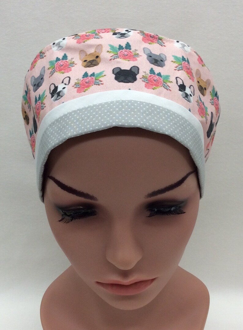 May include: A pink and white scrub hat with a pattern of French Bulldogs and flowers. The hat has a gray and white polka dot trim.