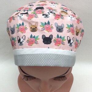 May include: A pink scrub hat with a white band and gray polka dot trim. The hat features a repeating pattern of French Bulldogs and pink flowers.