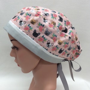 May include: A pink surgical scrub hat with a white and gray trim. The hat features a repeating pattern of French Bulldogs and flowers.