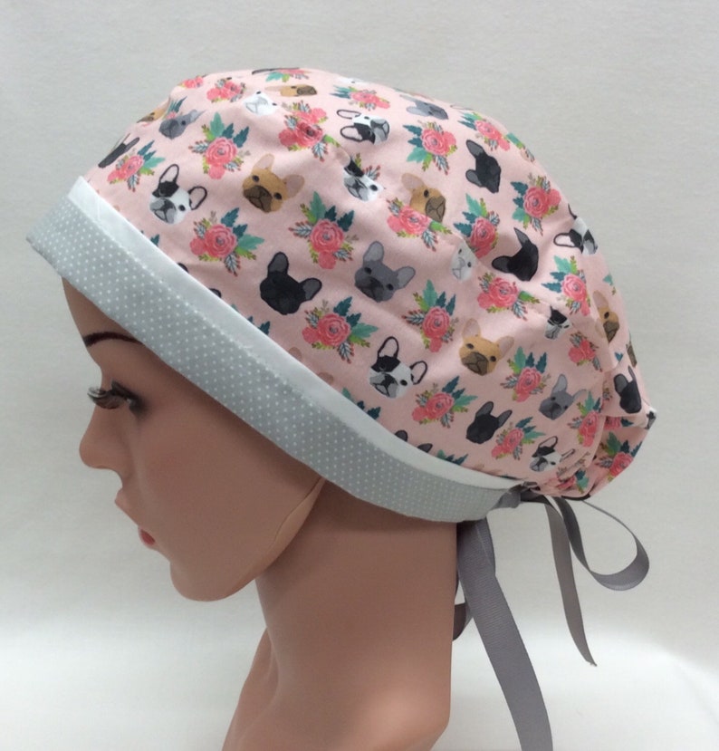 May include: A pink surgical scrub hat with a white and gray trim. The hat features a repeating pattern of French Bulldogs and flowers.