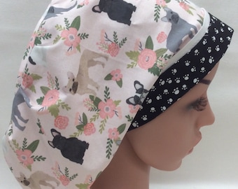 May include: A pink and white scrub hat with a floral pattern and a black and white paw print pattern on the underside. The hat features a variety of French bulldog illustrations.