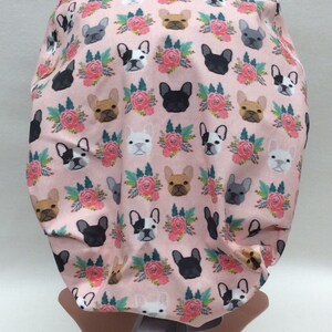 May include: A pink surgical scrub hat with a pattern of French Bulldogs and floral bouquets. The hat has a gray ribbon tie.