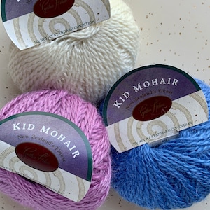 May include: Three balls of yarn in white, lavender, and blue. Each ball has a label that reads "Kid Mohair New Zealand's Finest Cynthia Helene 50g Net at Standard Condition."