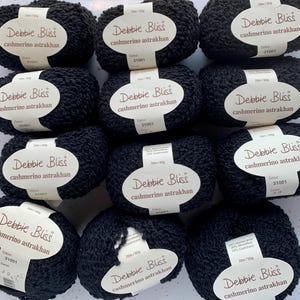 May include: A collection of black Debbie Bliss Cashmerino Astrakhan yarn balls. Each ball has a white label with the brand name, yarn type, and color code 31001. The yarn is a blend of merino wool and cashmere.
