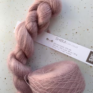 May include: A skein and a ball of soft, dusty rose-colored yarn. The yarn is labeled "SHIBUI/silk cloud" and is composed of kid mohair and silk. The label also indicates the yardage, weight, and needle size.