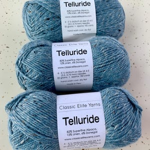 May include: Three skeins of blue yarn labeled "Telluride" with the yarn composition and care instructions. The yarn is 82% superfine alpaca, 12% linen, and 6% Donegal. The yarn is made by Classic Elite Yarns.