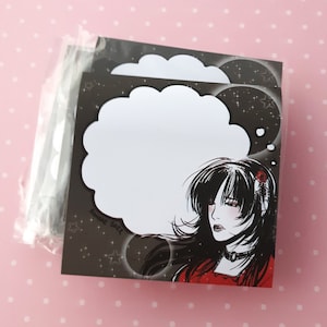 May include: A stack of black and white memo pads with a manga-style illustration of a woman with long black hair and red accents. The pads have a cloud-shaped blank space for notes, and a starry background.